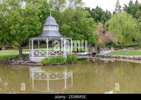 A white pagoda surrounded by trees and flowers on a large garden pond Stock Photo