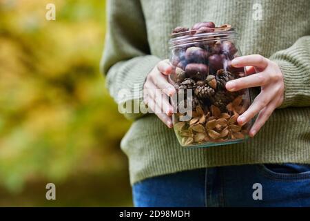 Close Up Of Girl Outdoors Holding Jar Of Autumn Pine Cones With Conkers Acorns And Beech Nut Cases Stock Photo