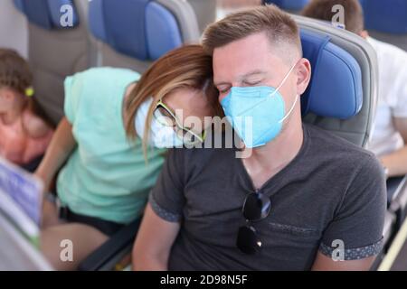 Man and woman in protective medical masks are sleeping on plane. Stock Photo