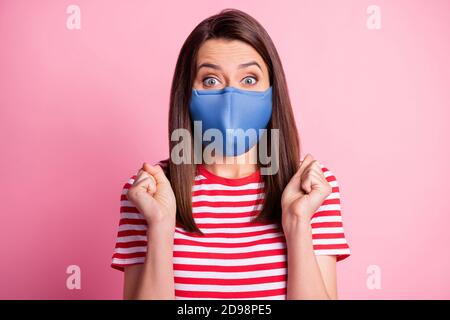 Photo portrait of happy brunette lady with fists in air wearing blue fabric face mask isolated on pastel pink colored background Stock Photo