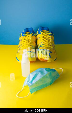 Overhead shot of fitness shoes, surgical mask and hydroalcoholic gel on a blue and yellow background. Concept of home fitness and new normal. Horizont Stock Photo
