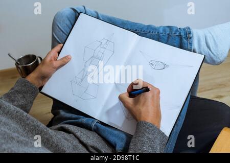 young male student taking notes. Hand drawing on a blank book on an armchair. over the shoulder view. Stock Photo