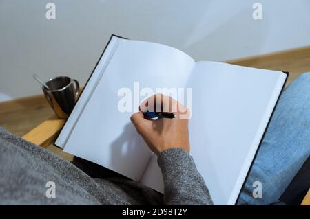 young male student taking notes. Hand drawing on a blank book on an armchair. over the shoulder view. Stock Photo