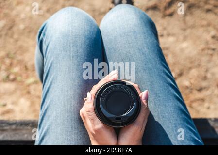 close up view of the top of a take away coffee cup with a warning about hot contents and hold by the hands of a unrecognizable young caucasian woman. Stock Photo