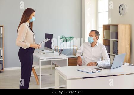 Company workers working together in the office wearing face masks and keeping social distance Stock Photo
