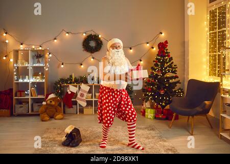 Funny grandpa wearing Santa beard and socks secretly putting present under Christmas tree at night Stock Photo