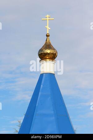 Orthodox Christian church with blue roof, golden dome and cross in Russia. A building for religious ceremonies with a bell tower against a cloudy sky. Stock Photo