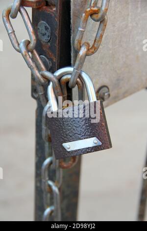 A new brown padlock with a shiny arc hangs on a chain on an iron door. Stock Photo