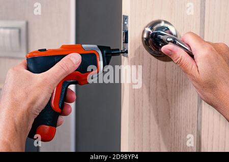 Repair of the door handle. The master clamps the loose screw with an electric screwdriver Stock Photo