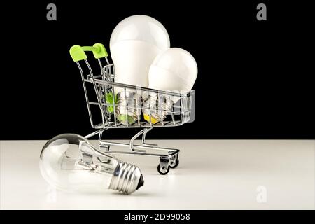 Energy-saving light bulbs are placed in a basket on wheels. A simple light bulb is lying on the table. The concept of modern economical lighting. Stock Photo