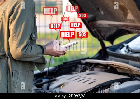 Young woman standing near broken car and using smartphone for help or assistance. Calling to car mechanic for auto repair. Stock Photo