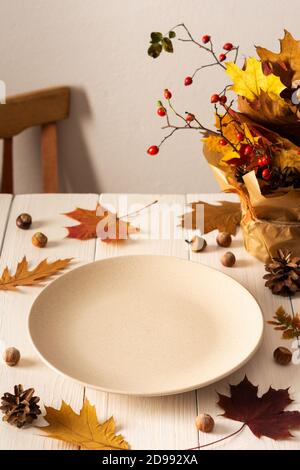 Autumn serving dish, empty plate on white wooden background, fall background with fallen maple and oak leaves, pine cones, rose hips and hazelnuts Stock Photo