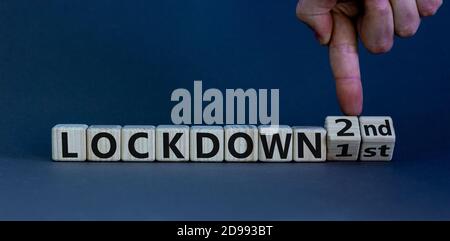 Symbol for a second lockdown. Hand turns cubes and changes the expression 'lockdown 1st' to 'lockdown 2nd'. Beautiful grey background. Medical and cov Stock Photo