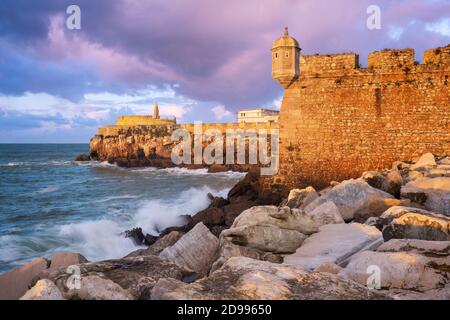 Peniche Fortress at sunset with beautiful golden light with sea waves crashing on the rocks, in Portugal Stock Photo