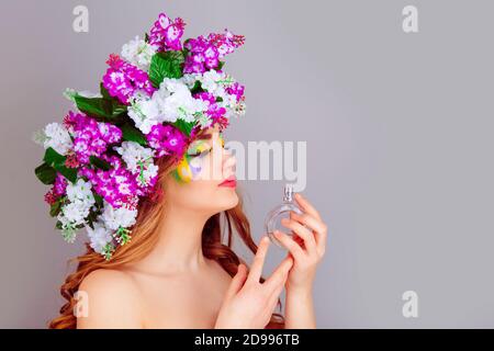 Closeup beautiful young woman in side profile with floral lilac headband smelling aroma of a perfume – isolated on light purple background. Positive h Stock Photo