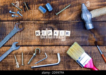 The word repair on wooden background. Nearby different working tools brush hammer wrench screwdriver. Stock Photo