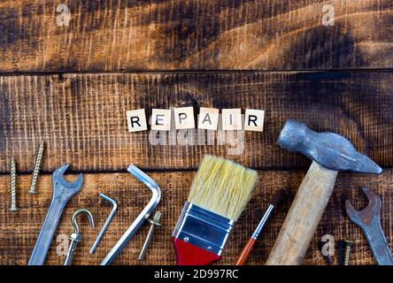 different working tools brush hammer wrench screwdriver. Repair word on wooden background. Stock Photo