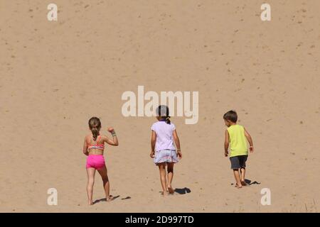 Three caucasian children climbing Sleeping Bear Dunes in Northern Michigan on a hot, sunny day Stock Photo