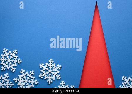 Christmas minimal concept with red christmas tree shape and white snowflakes on blue background. Copy space. View from above Stock Photo