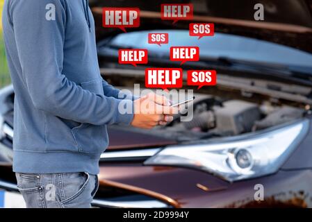 Young man standing near broken car and using smartphone for help or assistance. Calling to car mechanic for auto repair. Stock Photo