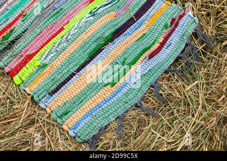 Colorful handmade knitted rug lays on hay, top view Stock Photo