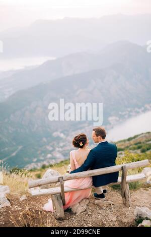bride and groom sitting on the bench on the mountain against the backdrop of the Bay of Kotor Stock Photo