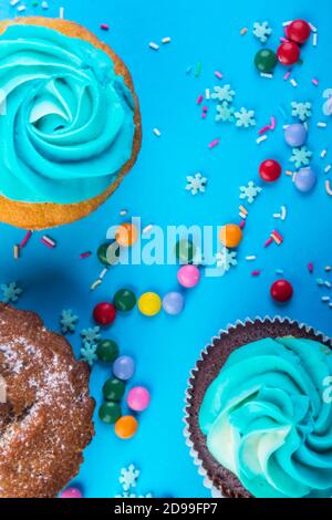 Gourmet chocolate and vanilla cupcakes topped with blue buttercream frosting, decorated with sprinkles on blue background, copy space, easter, christm Stock Photo
