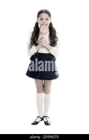 Rewarding herself with sweets. Food addictions. Girl kid eat sweet lollipop. Girl pupil school uniform like sweets lollipop candy white background. Healthy nutrition diet. Sweets reward for study. Stock Photo