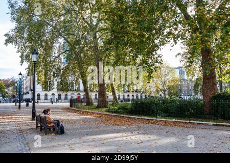 A couple sitting on a bench in Fitzroy Square  on a sunny afternoon in October during the Coronavirus pandemic, London, UK Stock Photo