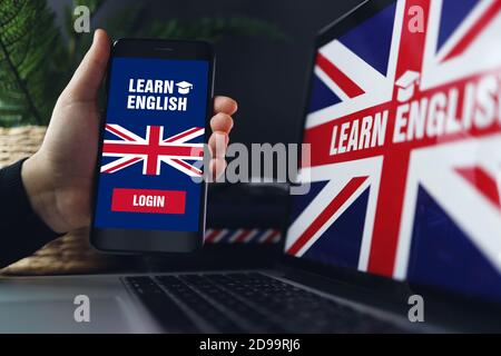 Learning foreign languages online. Woman holding smartphone with app for studying English on screen, copy space. Laptop with British flag in back. Stock Photo