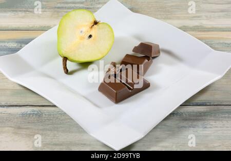Chocolate bar pieces with pear filling and fresh raw pear half on white snack plat Stock Photo