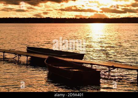 Trout Lake, Michigan, USA. A few remaining clouds mute the late afternoon sun as it reflects onto the lake's surface beyond a pair of rowboats. Stock Photo
