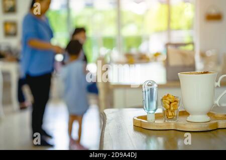 Mini portable alcohol gel bottle to kill Corona Virus(Covid-19) and biscuits and coffee cup on table with blurred image of a family eating at restaura Stock Photo