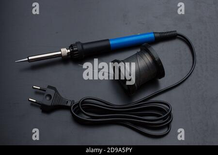 A soldering iron with a blue handle and a coil of solder on the old black desktop surface. Back light. Stock Photo