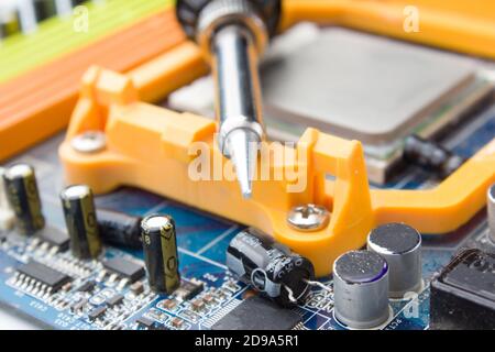 soldering iron on the background of a computer Board and capacitors in soft focus. The concept of repair and service Stock Photo