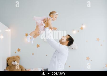 Father lifting baby girl. Happy father picks up and throws his lifting a small child. Home atmosphere, happy family laughing baby Stock Photo