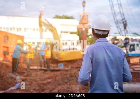 Engineer technician watching team of workers at construction site, Engineer technician Looking Up and Analyzing an Unfinished new construction Project Stock Photo