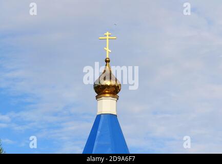 Orthodox Christian church with blue roof, golden dome and cross in Russia. A building for religious ceremonies with a bell tower against a cloudy sky. Stock Photo