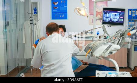 Oral surgeon performing surgery installing implant into senior woman mouth in dental clinic. Dentistry doctor wearing protection mask treating teeth of patient lying on chair with open mouth. Stock Photo