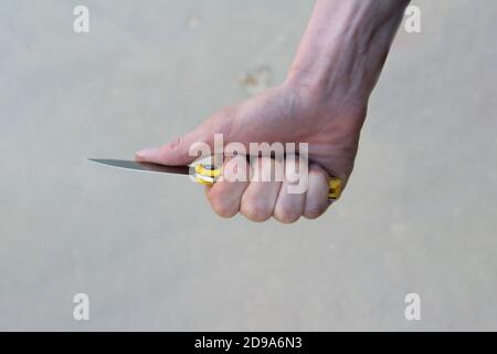 The man's hand holds a knife. Fingers compress a folding knife with a shiny close-up blade. The concept of crime, assault, weapons, security and attempted murder. Stock Photo