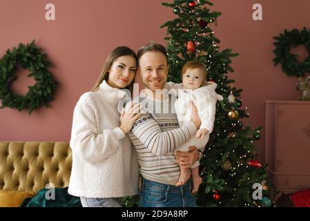 Family portrait of a stylish young family with a small child near the Christmas tree in the living room in their new home Stock Photo