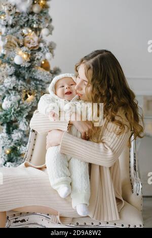 Happy family: a mother and young son sit on a chair during the Christmas holidays. New year holiday. Baby with mom in a festively decorated room with Stock Photo