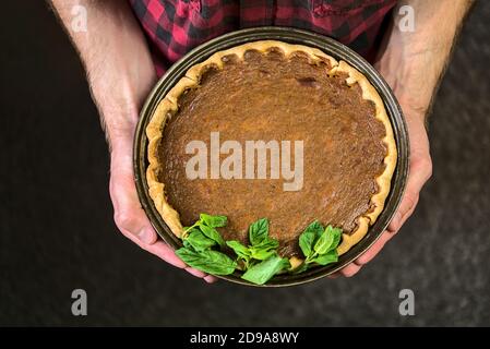 Beautiful young man hands holding delicious pumpkin pie with fresh mint leaves. Top view. Traditional dessert for Thanksgiving. Man cooking Stock Photo