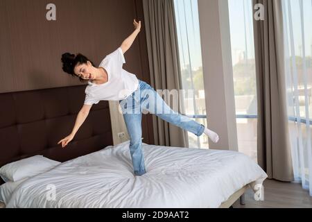 Happy young woman dancing on the bed in the bedroom. Windows on the background. Top view. Stock Photo