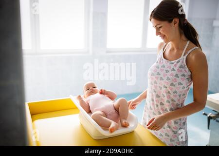 Mother weighting cute baby on scales in room Stock Photo