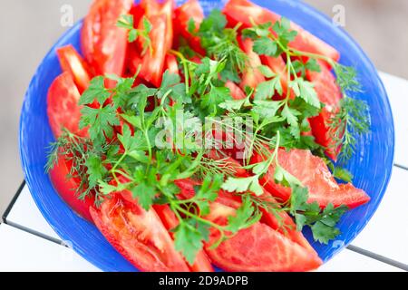 chopped tomato with parsley and dill on a blue plate Stock Photo