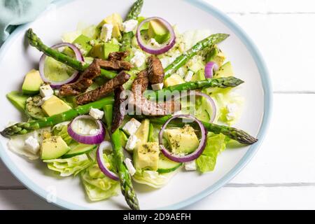 Asparagus salad with avocado, steak strips, red onion and lettuce on white table with space for text Stock Photo