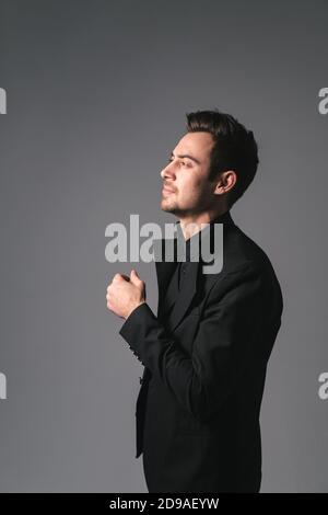 Studio portrait of a young caucasian man in a black blazer, looking to the side, standing half-turned against plain studio background Stock Photo