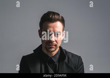 Studio portrait of a young caucasian man in a black blazer, looking at the camera, against plain studio background Stock Photo