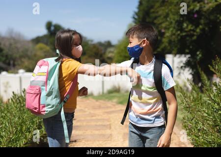 Caucasian boy and girl wearing face masks greeting on their way to school by touching elbows Stock Photo